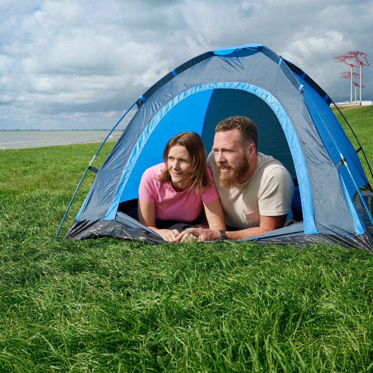 Paar liegt entspannt im Zelt auf einer Wiese mit Blick aufs Wasser – Symbol für Sicherheit, Geborgenheit und zuverlässige Energieprodukte von GEW Wilhelmshaven.
